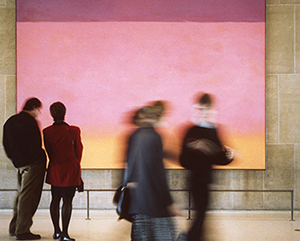 People pass in front of a large pink and orange painting in the Law School's Green Lounge