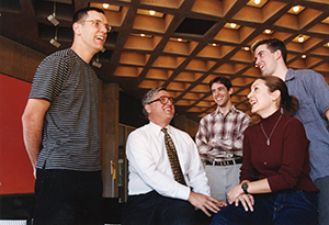 Daniel Fischel, in a white button-up shirt and tie, with glasses, is surrounded by smiling students.