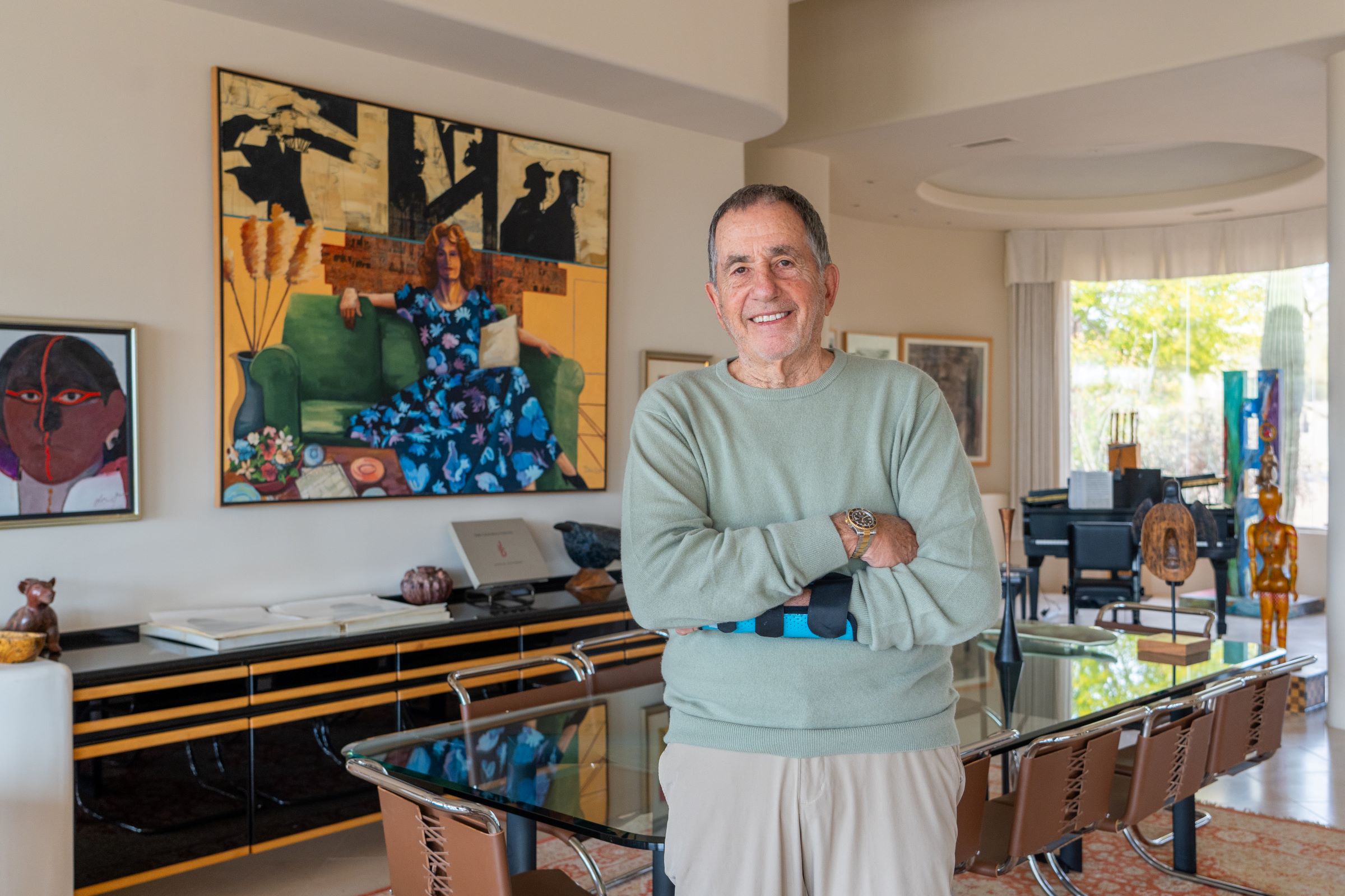 A man standing in a wide open room with a dining table behind him and colorful art on the walls.