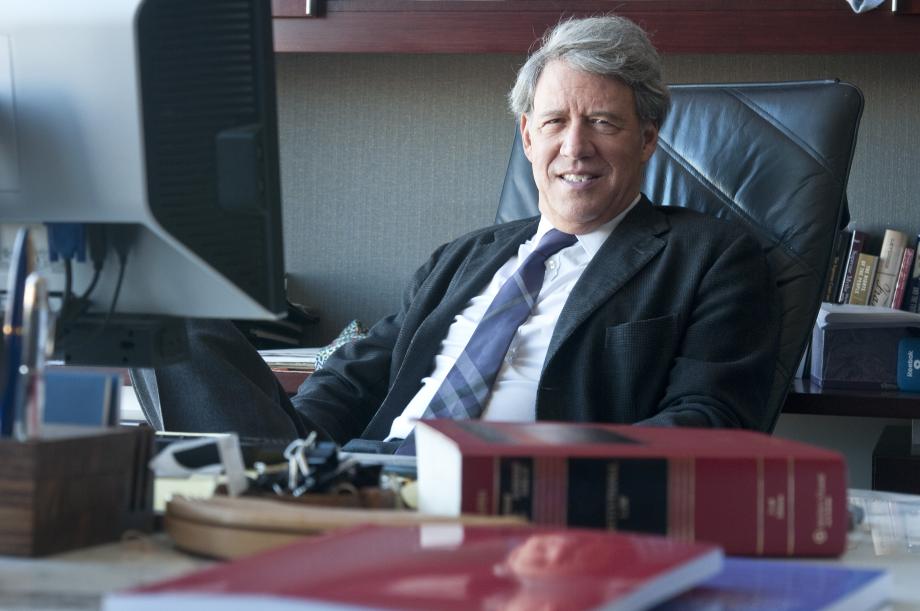 Stone, in a suit, sits at his desk with a casebook in front of him.