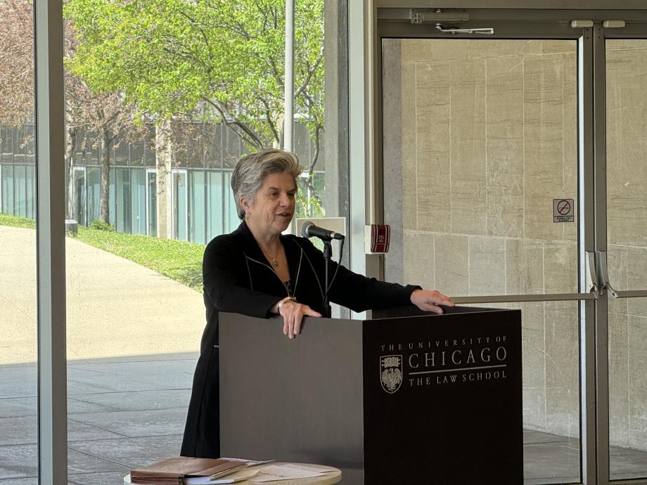 Julie Justicz, wearing a black dress and gold necklace, speaking at the podium.