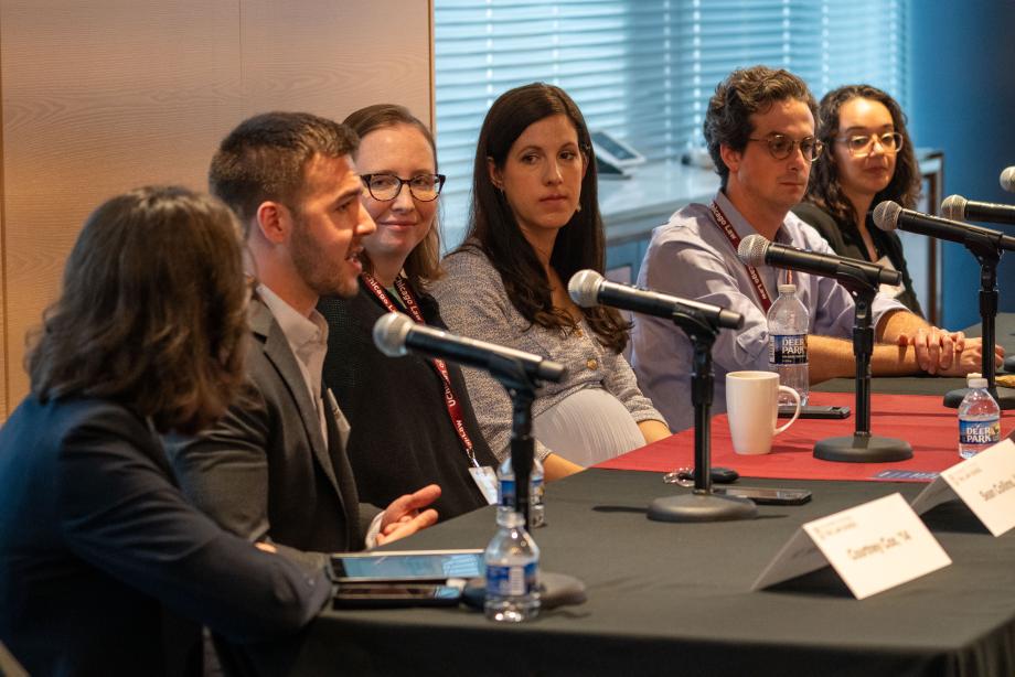 Five panelists sit a table draped with a University of Chicago Law School tablecloth. One panelist, in a beige suit jacket speaks into the tabletop microphone while the other panelists look on.