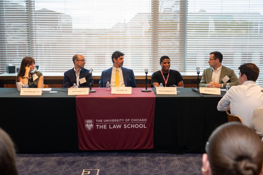 Five panelists sit a table draped with a University of Chicago Law School tablecloth. One panelist, in a black sweater speaks into the tabletop microphone while the other panelists look on.