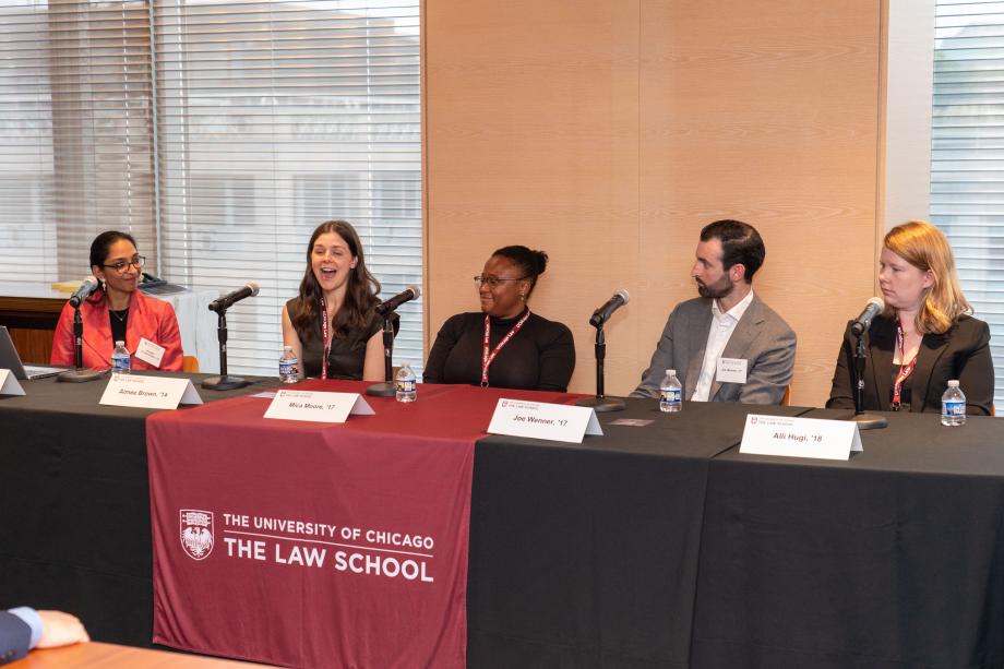 Five panelists sit a table draped with a University of Chicago Law School tablecloth. One panelist, in a black blouse speaks into the tabletop microphone while the other panelists look on.