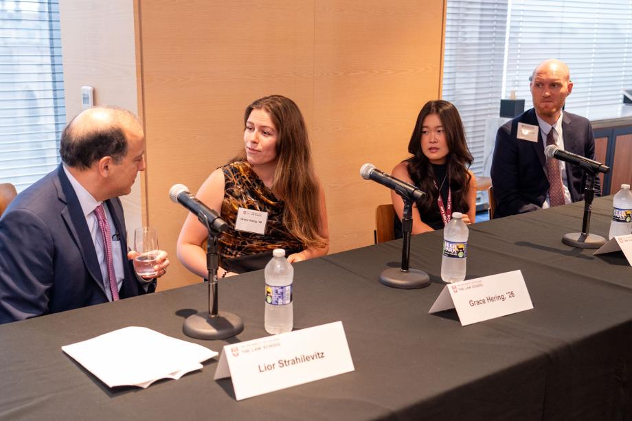 Four panelists sit a table draped with a University of Chicago Law School tablecloth. One panelist, wearing an orange, gold, and black blouse looks at the panelist to their left while preparing to speak.