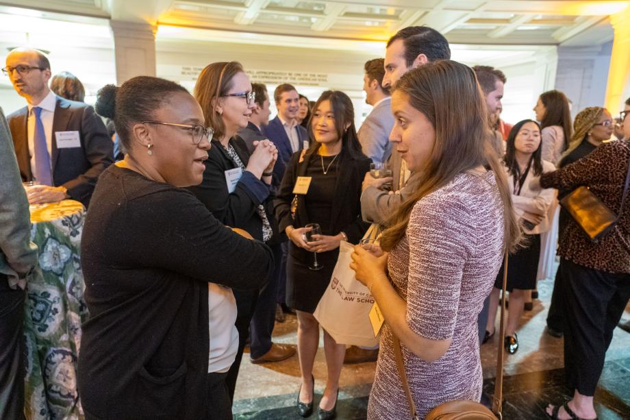 Two people facing each other chatting in the foreground with other attendees mingle in the background.