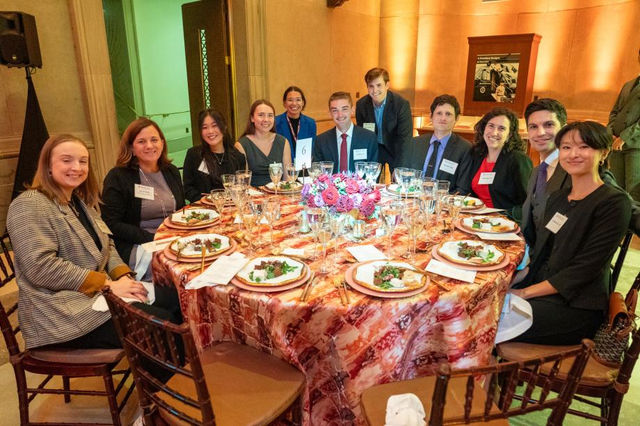 Attendees seated at a large circular table with salad plates in front of each person. The attendees crowd around the further half of the circular table to pose for the picture with smiles.