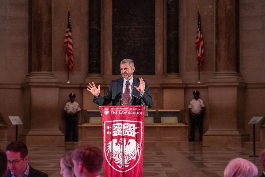 Dean Thomas Miles standing at a podium draped with the UChicago logo and shield inside the National Archives Museum event space. Miles faces the audience of attendees while speaking and gesturing his hands forward.