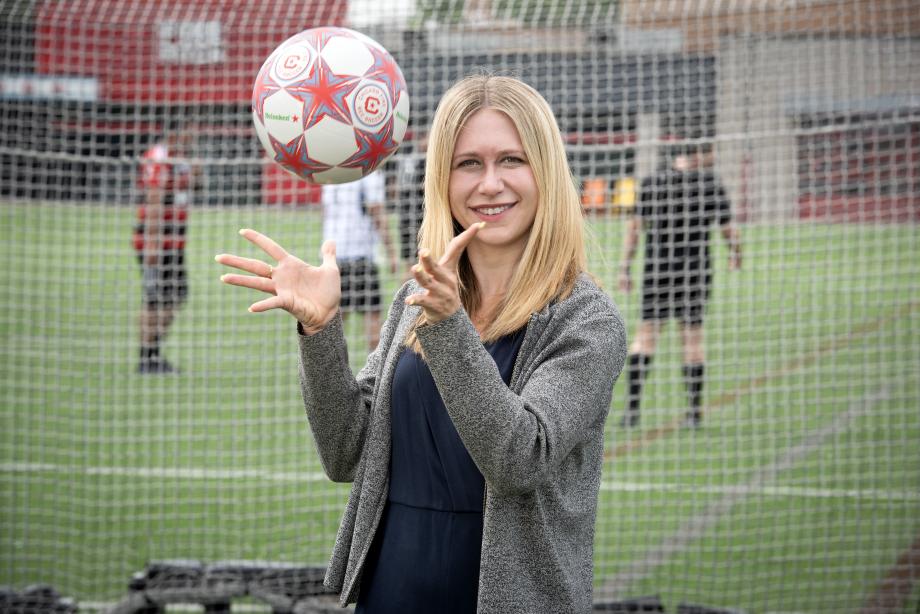 Shelby Klose stands in front of the net of a soccer goal as she throws a soccer ball in the air.