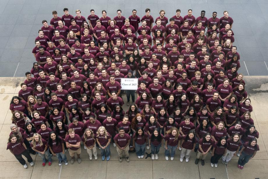 An aerial shot of a group of students standing together shoulder to shoulder wearing maroon shirts and holding a sign that says class of 2027