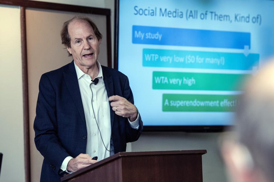 A man stands at a lectern delivering a talk with a screen behind him.