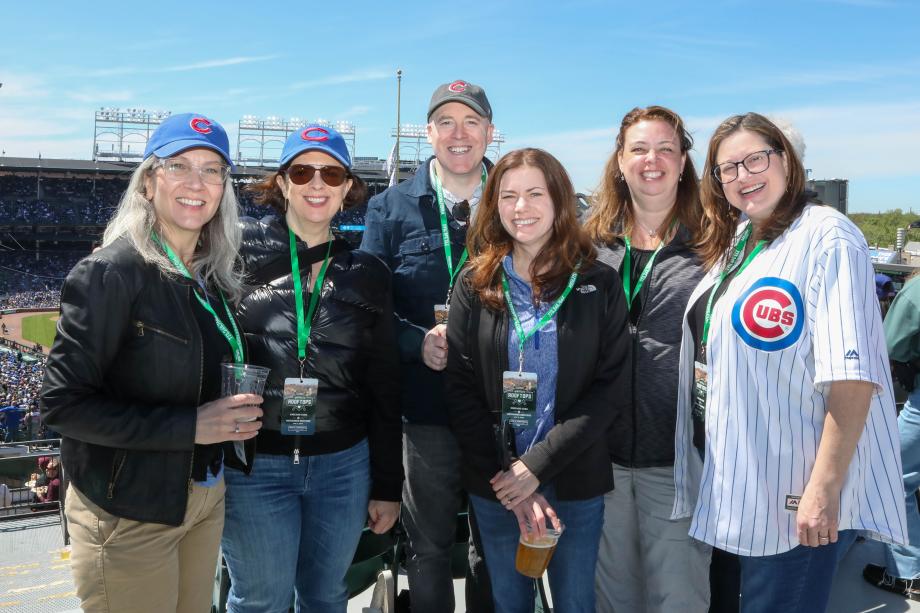 A small group of people standing together on the rooftop of a baseball stadium, smiling under a bright blue sky.