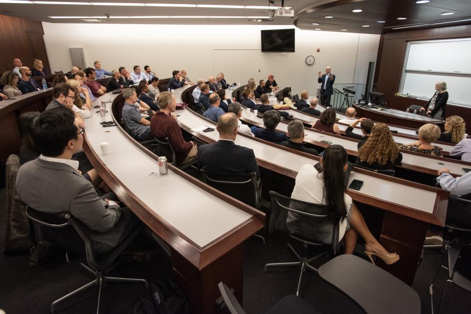 A classroom filled with people listening to a man and a woman talking at the front of the room.