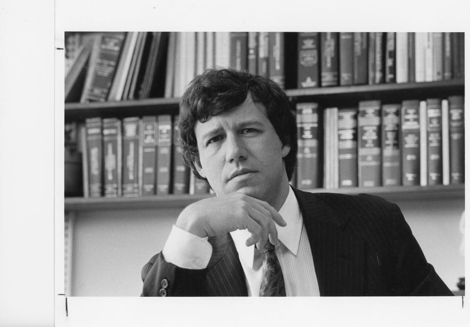 Stone, in a suit, looks into the camera with rows of books behind him.