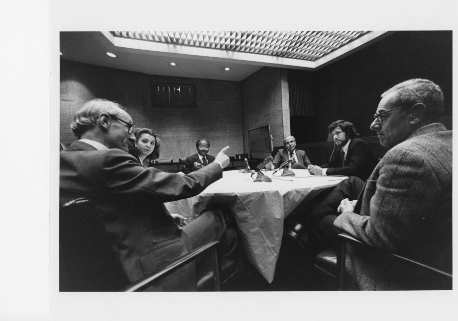 Five men and one women huddle around a round table.