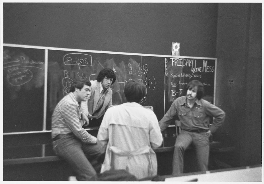 Geoffrey Stone returned to teach at the Law School only two years after graduating. Four people huddle in front of a blackboard in a classroom.