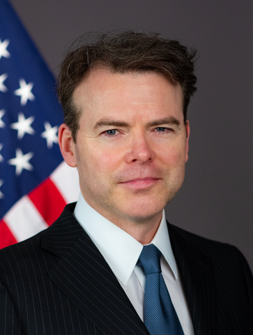 Headshot of a man wearing a suit and standing in front of the American flag