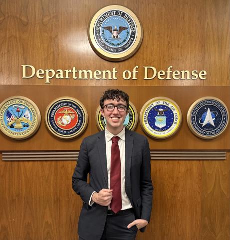 Robert Dorhman stands in front of a wood-paneled wall with Department of Defense emblems.