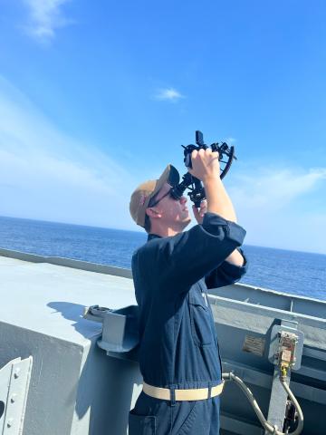 On a boat, Matt Davis looks into a sextant.