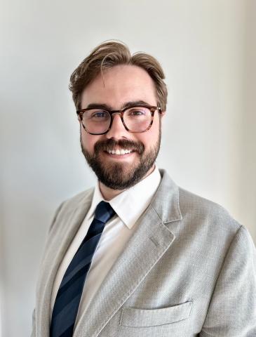 Zachary Brown smiles at the camera in a light grey suit and tie.