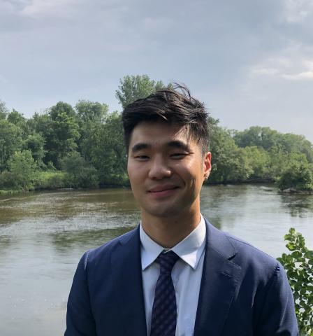 A man wearing a suit and smiling with a view of a river in the background