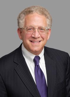 Professional headshot of Jonathan Blum in a pinstripe suit and purple tie.