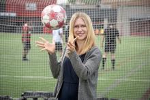 Shelby Klose stands in front of the net of a soccer goal as she throws a soccer ball in the air.