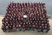 An aerial shot of a group of students standing together shoulder to shoulder wearing maroon shirts and holding a sign that says class of 2027